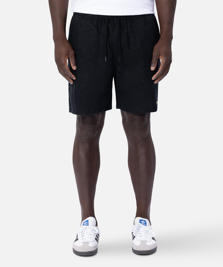 A model from the waist down wearing black drawstring shorts and white sneakers, standing against a light gray studio background.