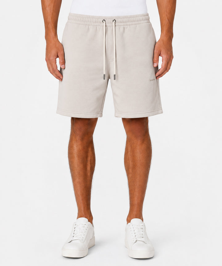 A model wearing light beige fleece drawstring shorts and white sneakers, shown from the waist down against a clean white background.