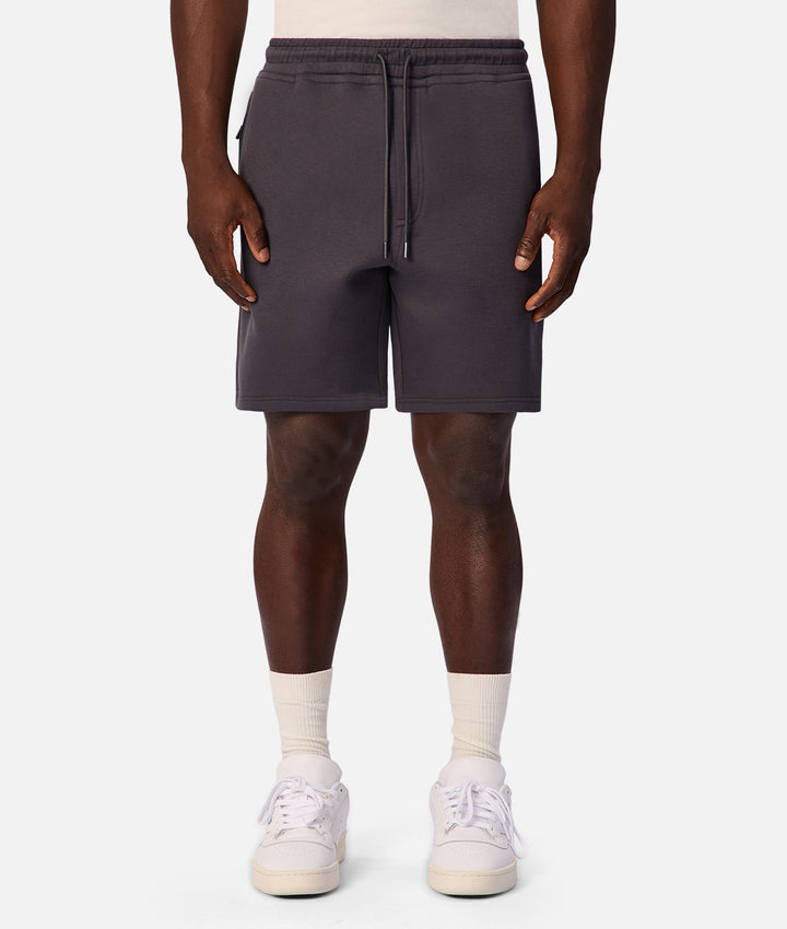 A person wearing dark charcoal gray drawstring shorts, white crew socks, and white sneakers, shown from the waist down against a light gray studio background.