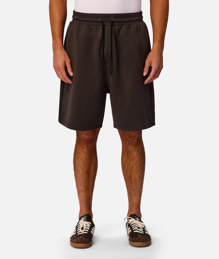 A person wearing dark brown drawstring shorts, shown from the waist down against a light gray studio background.