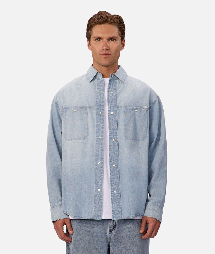 Man wearing a light blue denim shirt over a white shirt on a white background