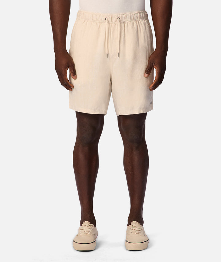 A model from the waist down wearing light beige drawstring shorts, dark brown tights, and beige platform sneakers against a light gray background.