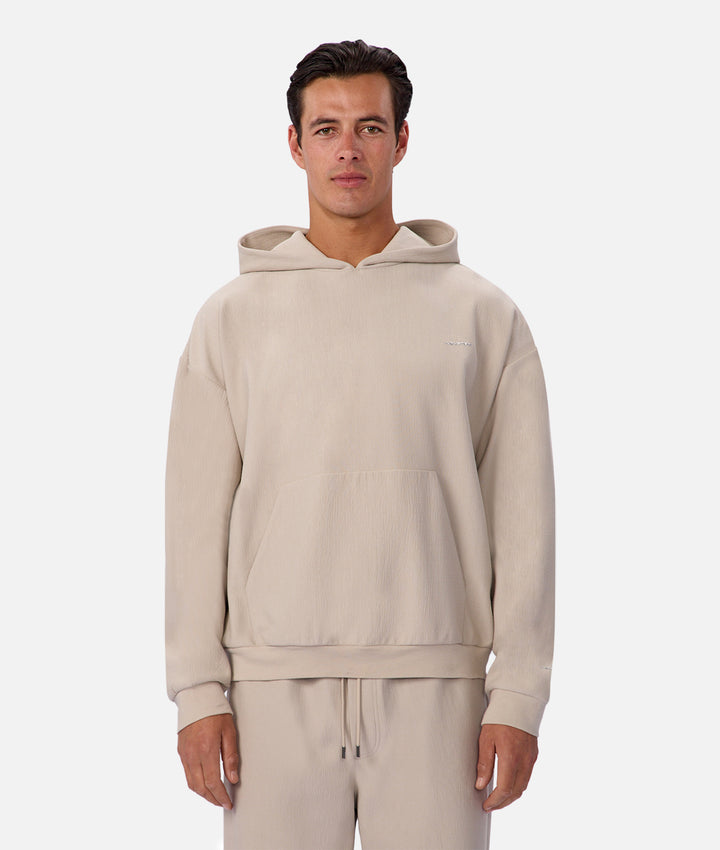 Man wearing a beige hoodie and pants on a white background