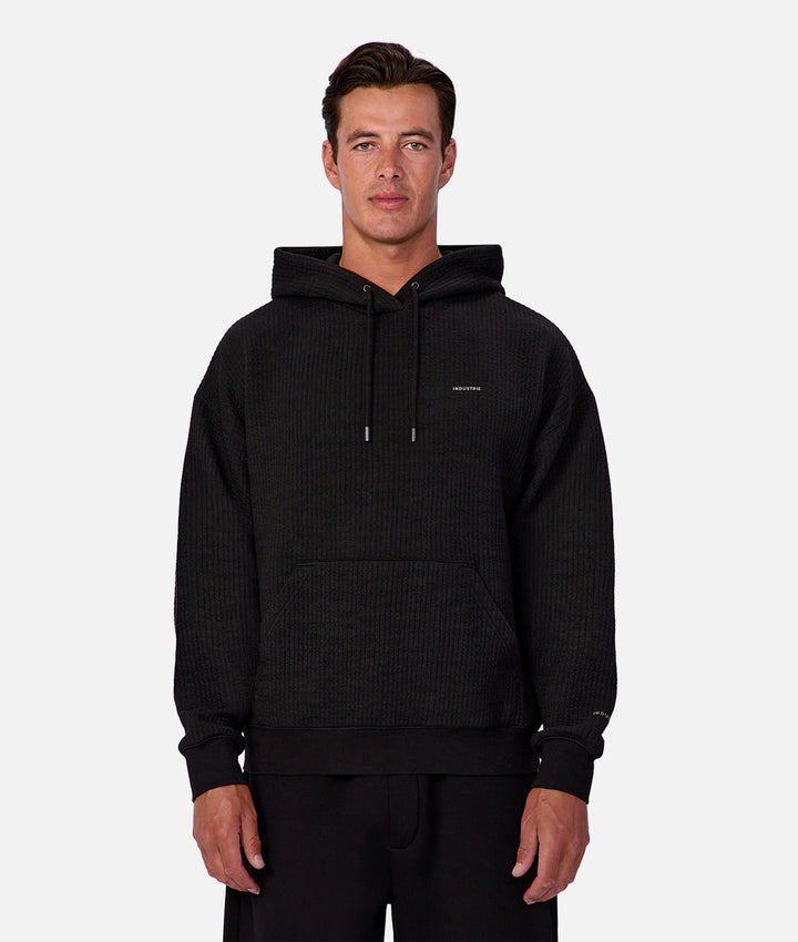 Man wearing a black textured hoodie with a brand logo on a white background