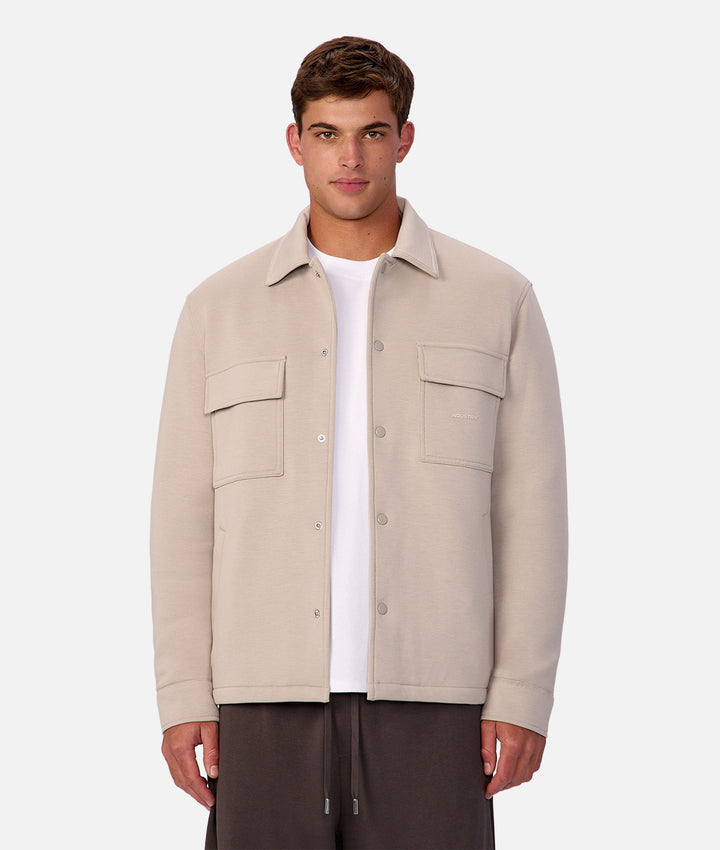 Man wearing a beige jacket over a white shirt on a light gray background