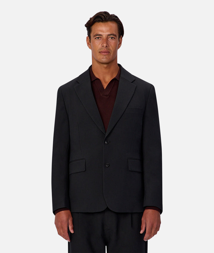 Man wearing a black suit jacket over a red shirt on a white background