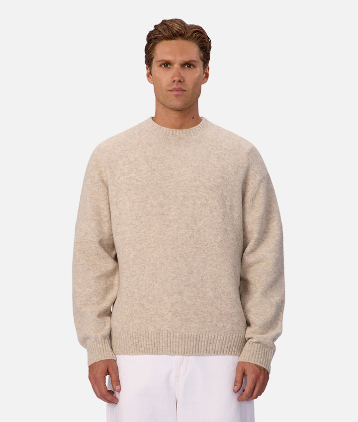 Man wearing a beige sweater and white pants on a light gray background