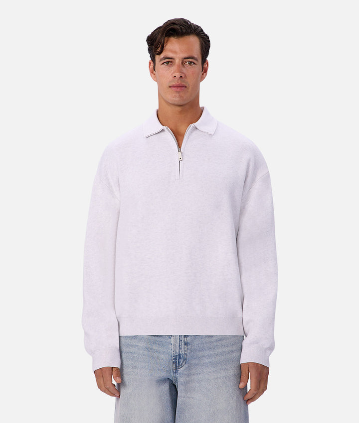 Man wearing a white long-sleeve shirt with a quarter zip and light blue jeans on a white background