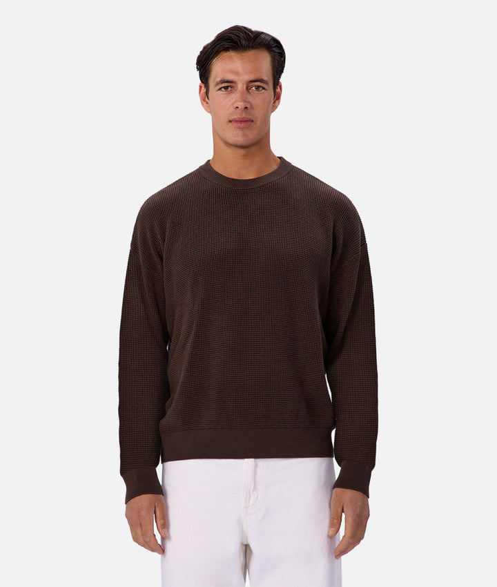 Man wearing a brown sweater and white pants on a white background