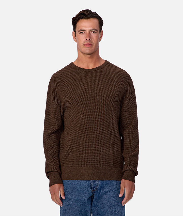 Man wearing a brown sweater and blue jeans on a white background