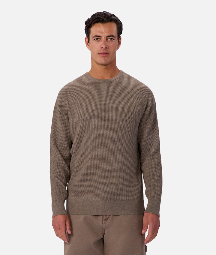 Man wearing a brown sweater and brown pants on a white background