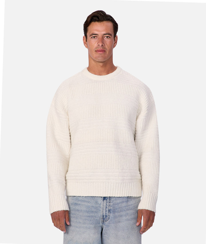 Man wearing a white sweater and light blue jeans on a white background