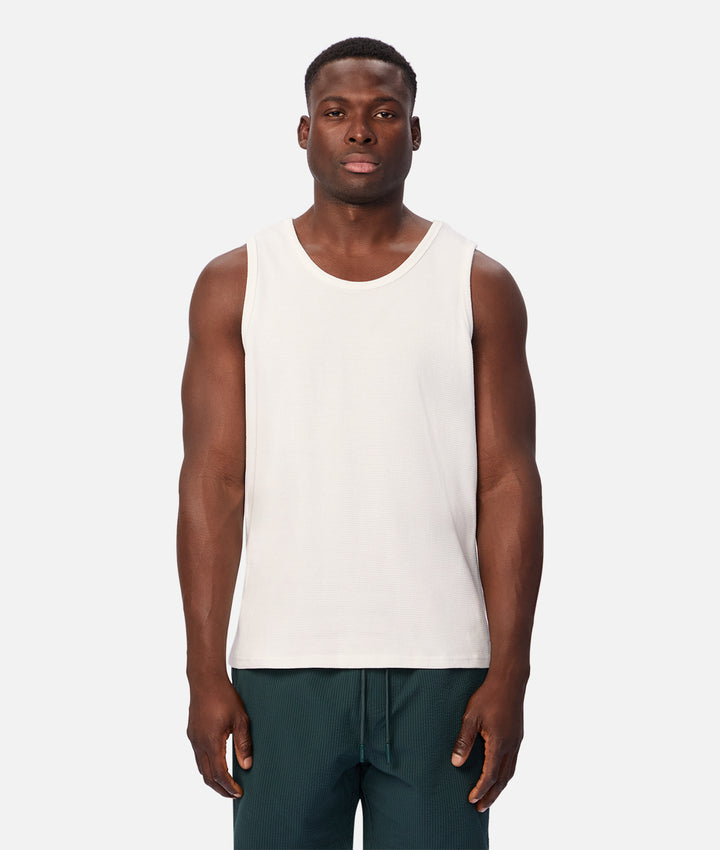 A man modeling a sleeveless white tank top against a light gray studio background.