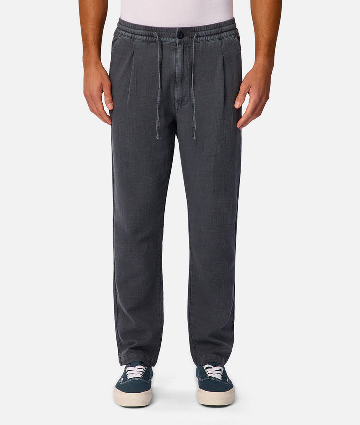 A person wearing dark gray drawstring jogger pants with a light pink top and navy sneakers, shown from the waist down against a light gray studio background.