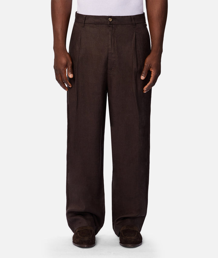 A person wearing dark brown wide-leg trousers with a white top and dark brown shoes, shown from the waist down against a light gray studio background.