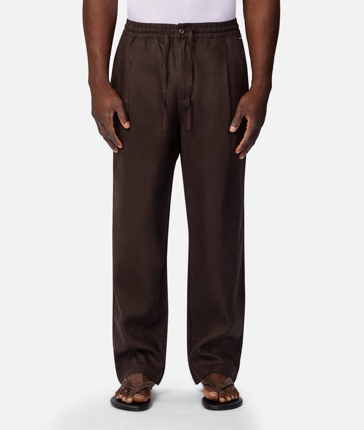A person wearing dark brown wide-leg drawstring pants with an elastic waistband, paired with brown leather sandals and a white top, shown against a light gray studio background.