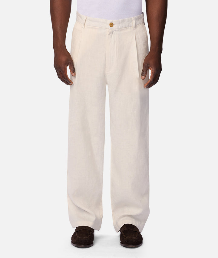 A person wearing off-white wide-leg trousers with a single gold button at the waist, paired with dark brown suede loafers against a light gray studio background.