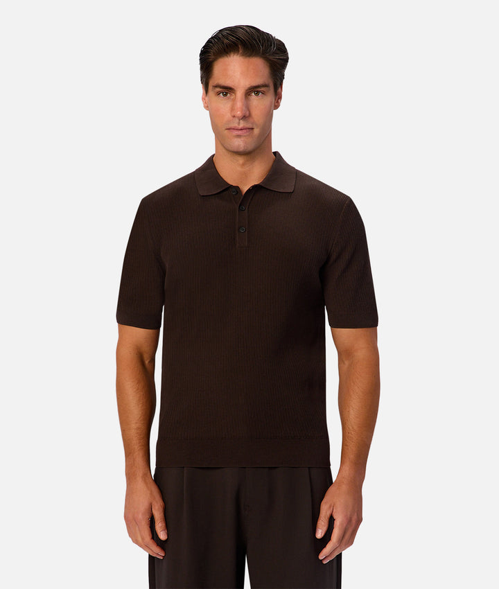 A man modeling a dark brown short-sleeve knit polo shirt against a light gray studio background.