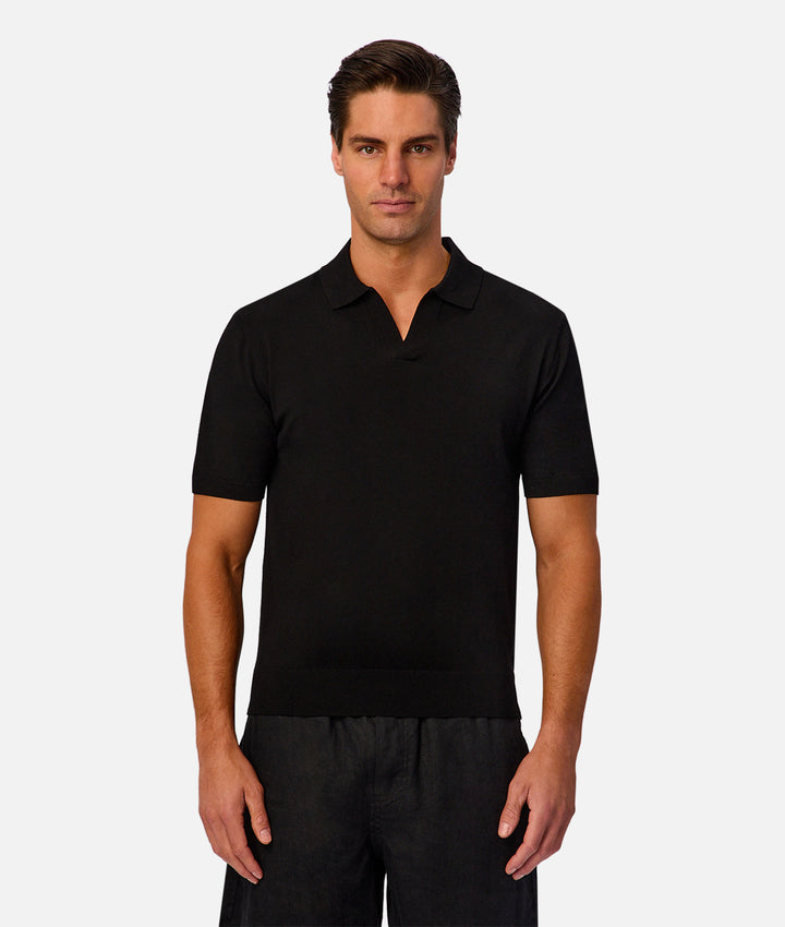 A man modeling a black short-sleeve polo shirt against a light gray studio background.