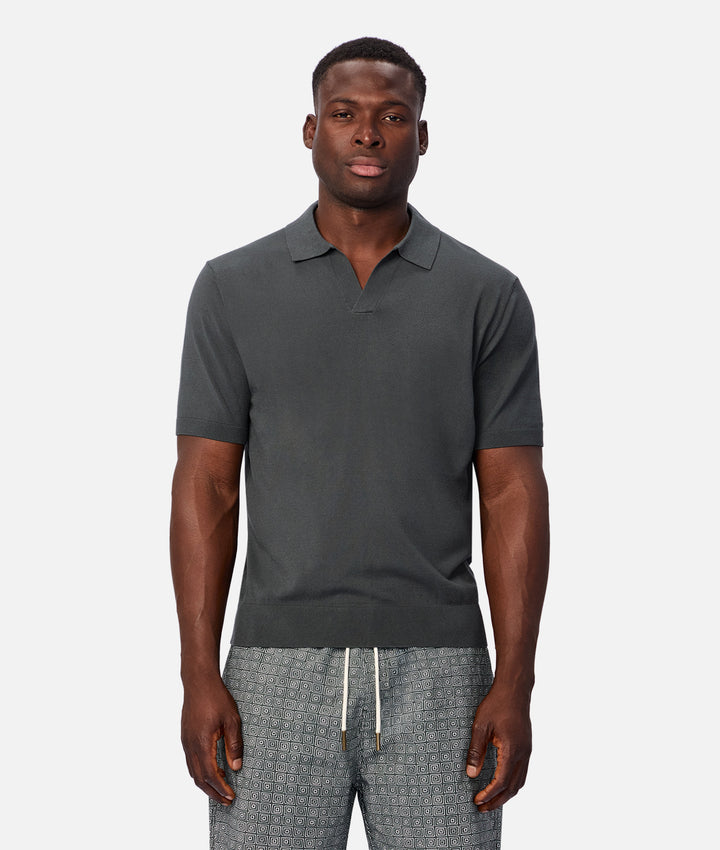 A man wearing a dark gray short-sleeve polo shirt and patterned gray drawstring pants, standing against a light gray studio background.