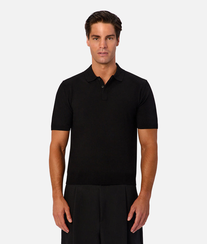 A man modeling a black short-sleeve polo shirt against a light gray studio background.