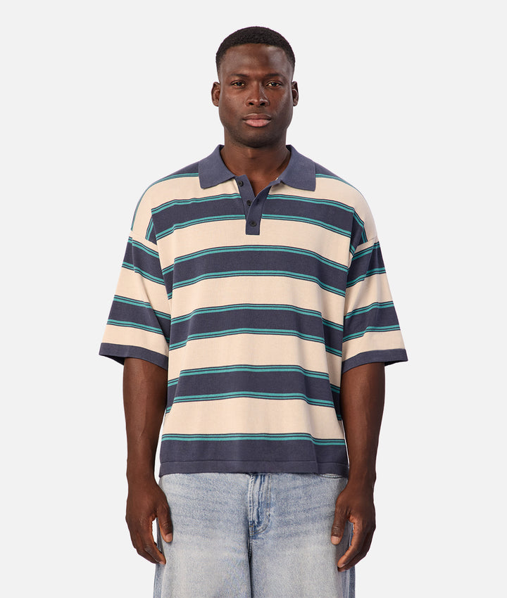 A man wearing a short-sleeve polo shirt with horizontal navy, teal, and cream stripes, paired with light-wash jeans, standing against a light gray background.