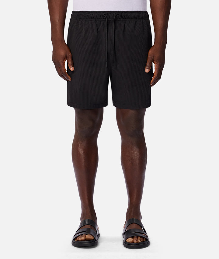 A model from the waist down wearing black athletic shorts with a drawstring waist, paired with black sandals, against a light gray studio background.