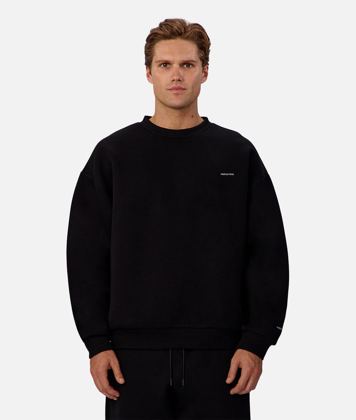 Man wearing a black sweatshirt with a small logo on a white background