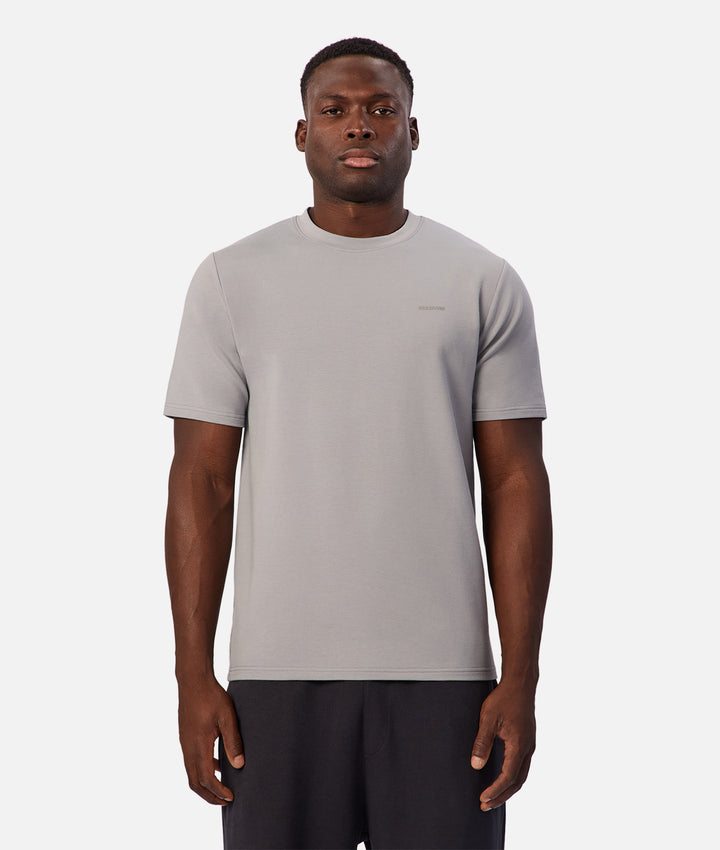 A man wearing a light gray crew-neck t-shirt and dark gray athletic shorts, standing against a solid light gray background.