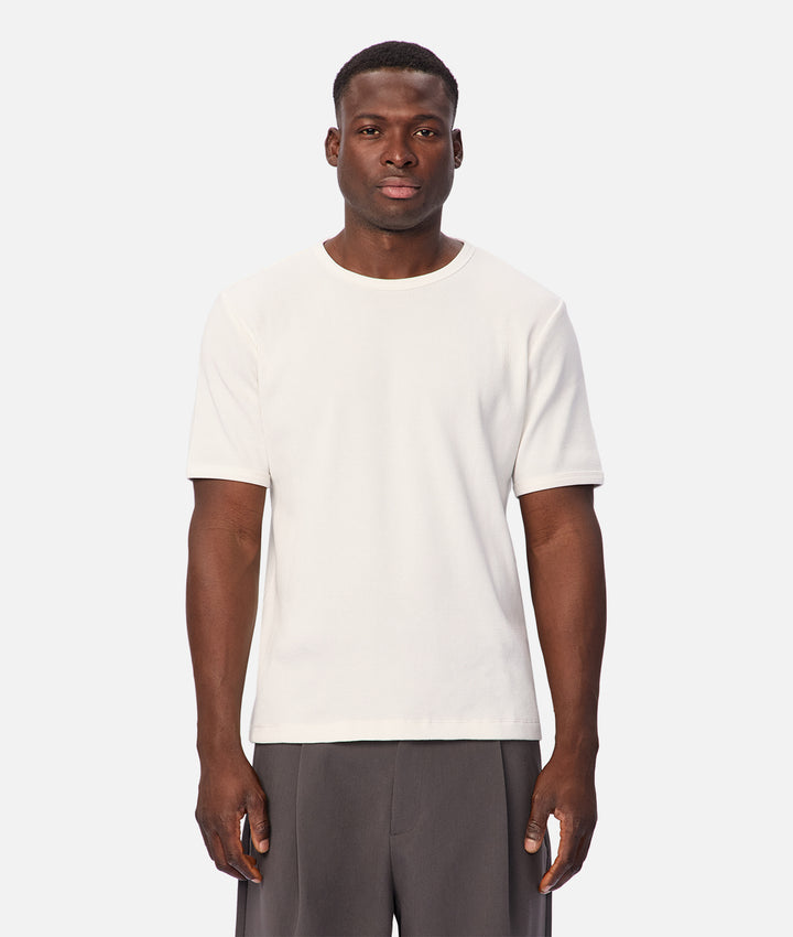 A man modeling a plain off-white short-sleeve crewneck t-shirt against a light gray studio background.