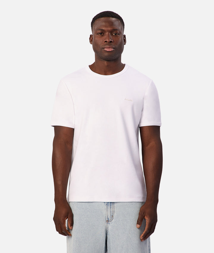 A man wearing a plain white short-sleeve crewneck t-shirt and light blue jeans, standing against a solid light gray background.