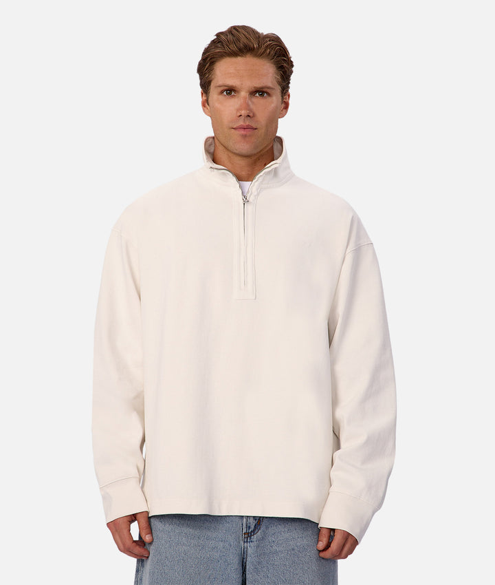 Man wearing a cream-colored half-zip sweatshirt on a white background